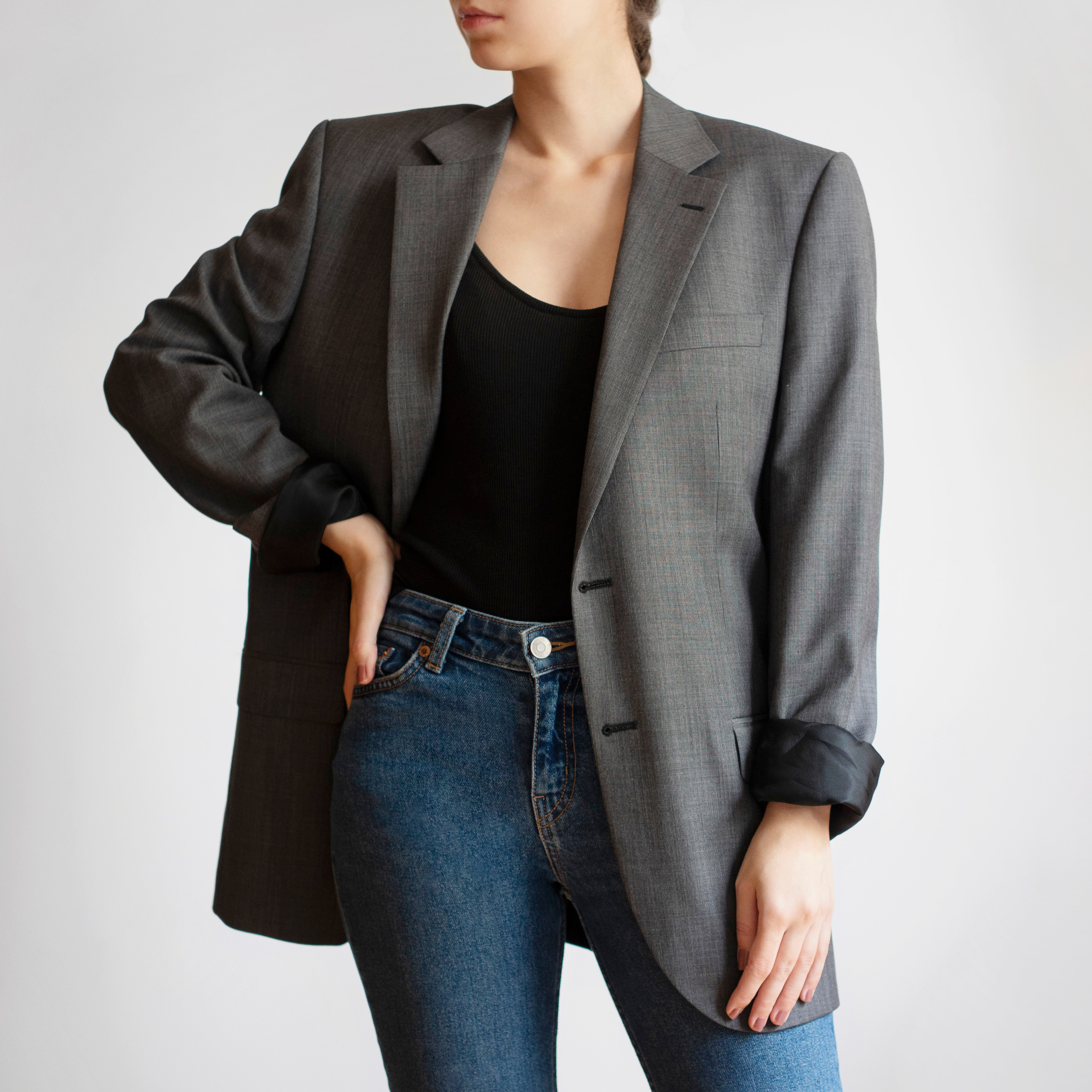 Une femme porte un jean et un t-shirt noir accessoirisé avec un blazer oversize gris