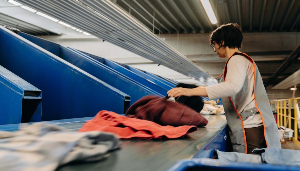 Une femme organise des vêtements sur un tapis roulant, effectuant un tri minutieux des articles.
