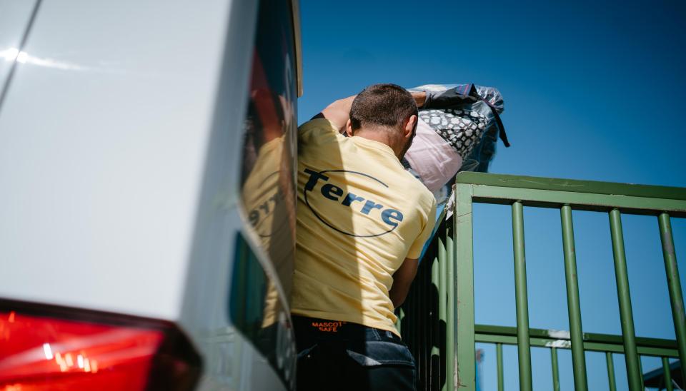 Un collecteur vide une camionnette remplie de sacs de vêtements.