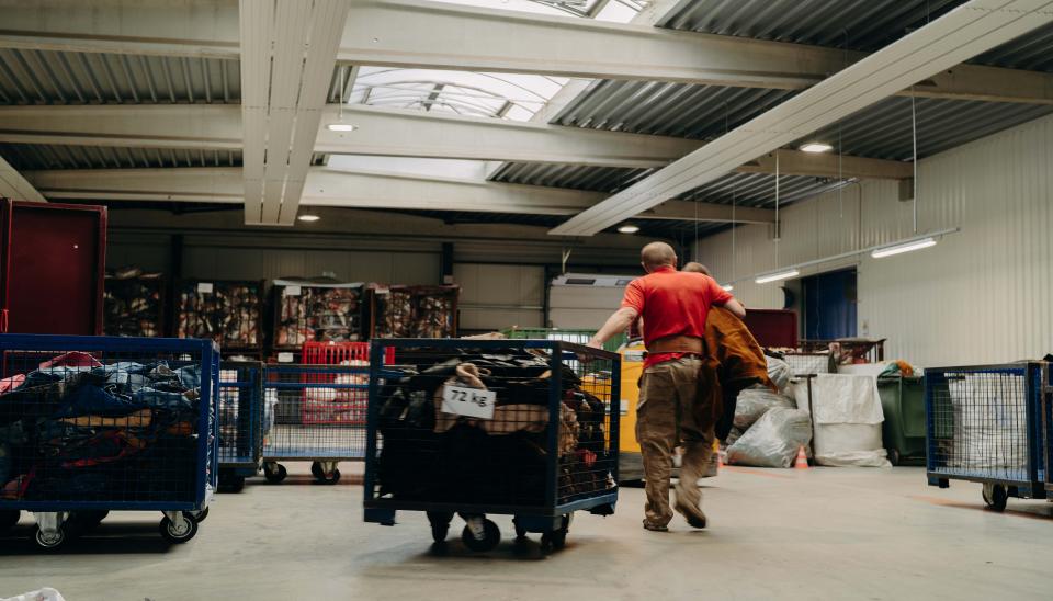 Un homme dans un grand hangar qui tire une cage remplie de textiles