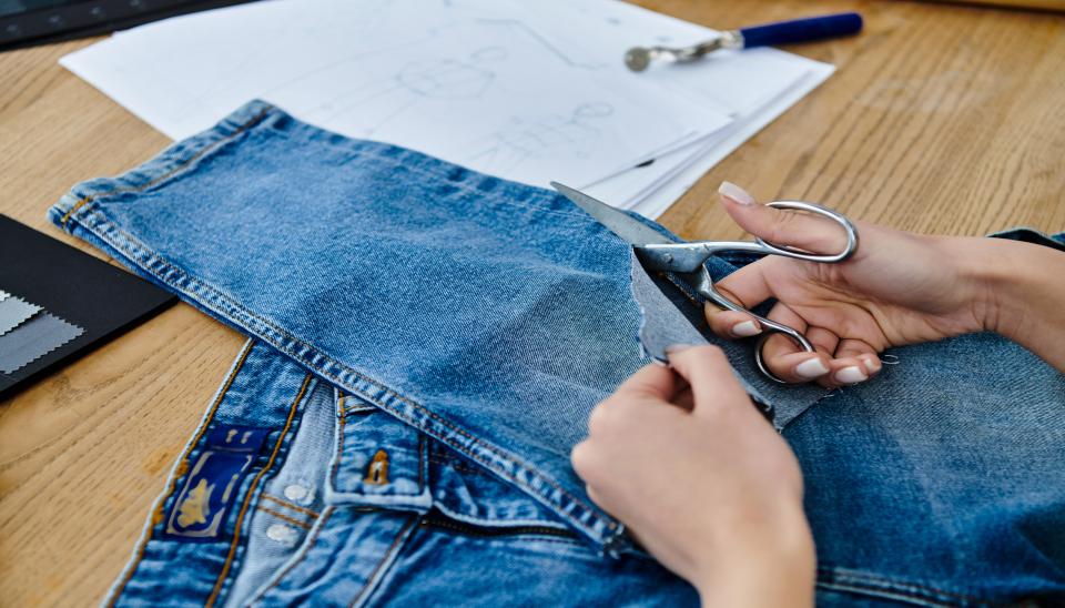 Des mains découpent dans un jean avec des ciseaux de couture