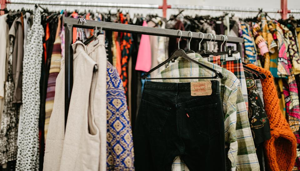 Des vêtements sur cintres accrochés à une tringle dans un magasin de vêtement de seconde main