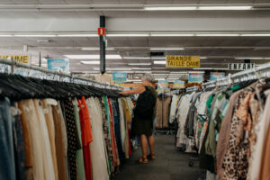 Une dame cherche un vêtement dans les rayons d'un magasin de seconde main